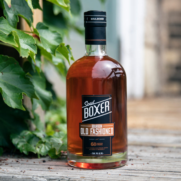 A bottle of the soulboxer bourbon old fashioned in front of a wall.