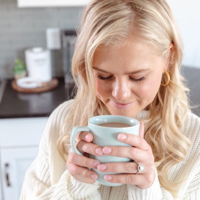 A blonde girl smiling while looking down at a cup of twi hot cocoa.