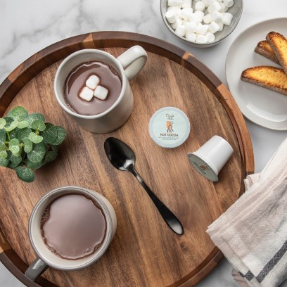 An overhead shot of two mugs of twi hot cocoa on a wooden platter.