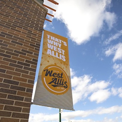 A sign hanging from a building that says That's Why West Allis.
