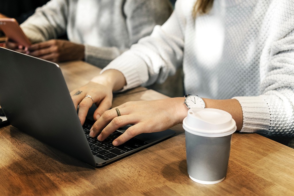 Hands typing on a computer next to a coffee cup.