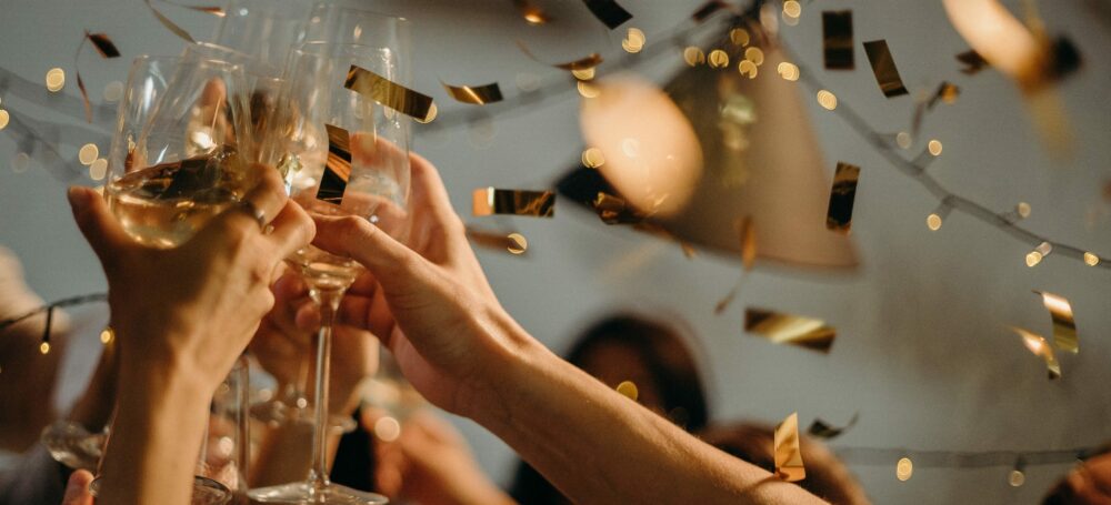 People cheer-sing champagne glasses while confetti falls from the ceiling.
