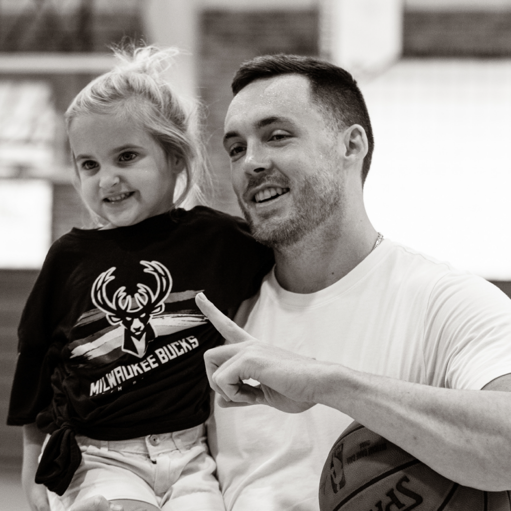 Pat Connaughton smiling while holding a young basketball camper.